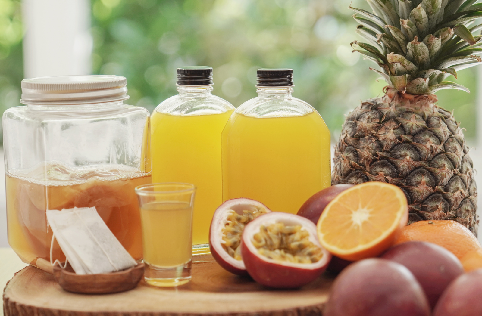 kombucha starter in jar with juices in jar and glass and passion fruit, orange and pineapple and tea ingredients