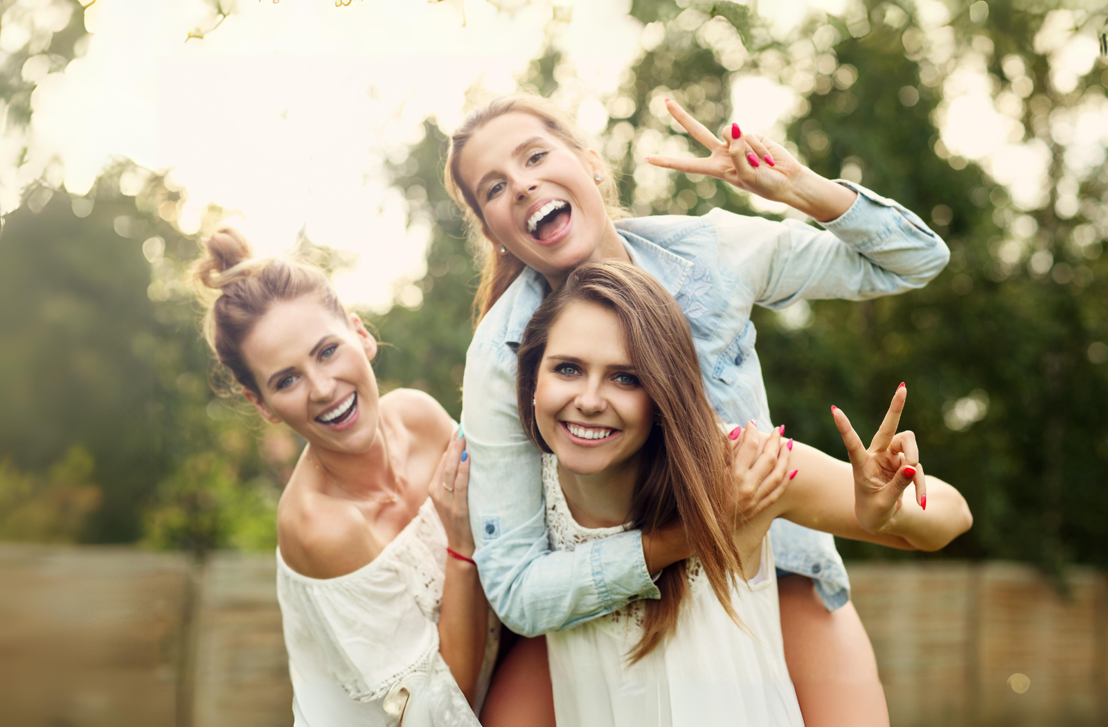 three girls, one is piggyback riding another girl and doing peace sign and one is beside there happy girls