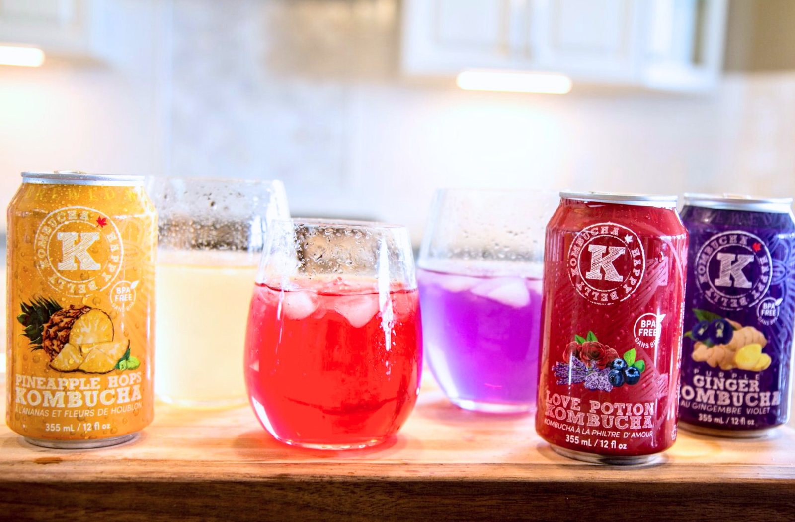 happy belly kombucha pineapple hops, love potion and purple ginger kombucha brewed flavors cans and three cocktail glasses drinks