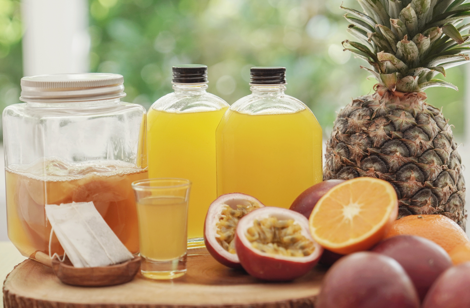 kombucha starter in jar with  juices in jar and glass and passion fruit, orange and pineapple and tea ingredients