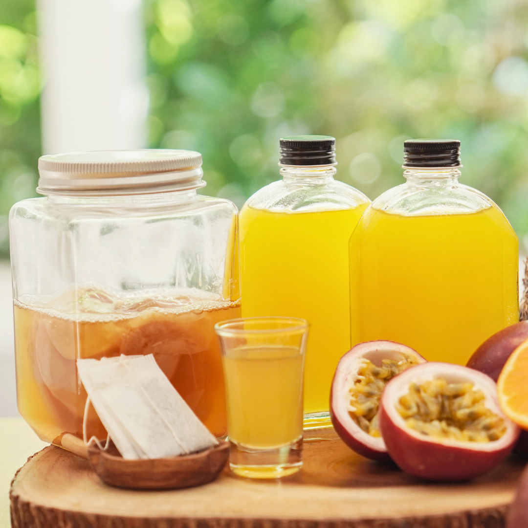 kombucha starter in jar with  juices in jar and glass and passion fruit, orange and pineapple and tea ingredients