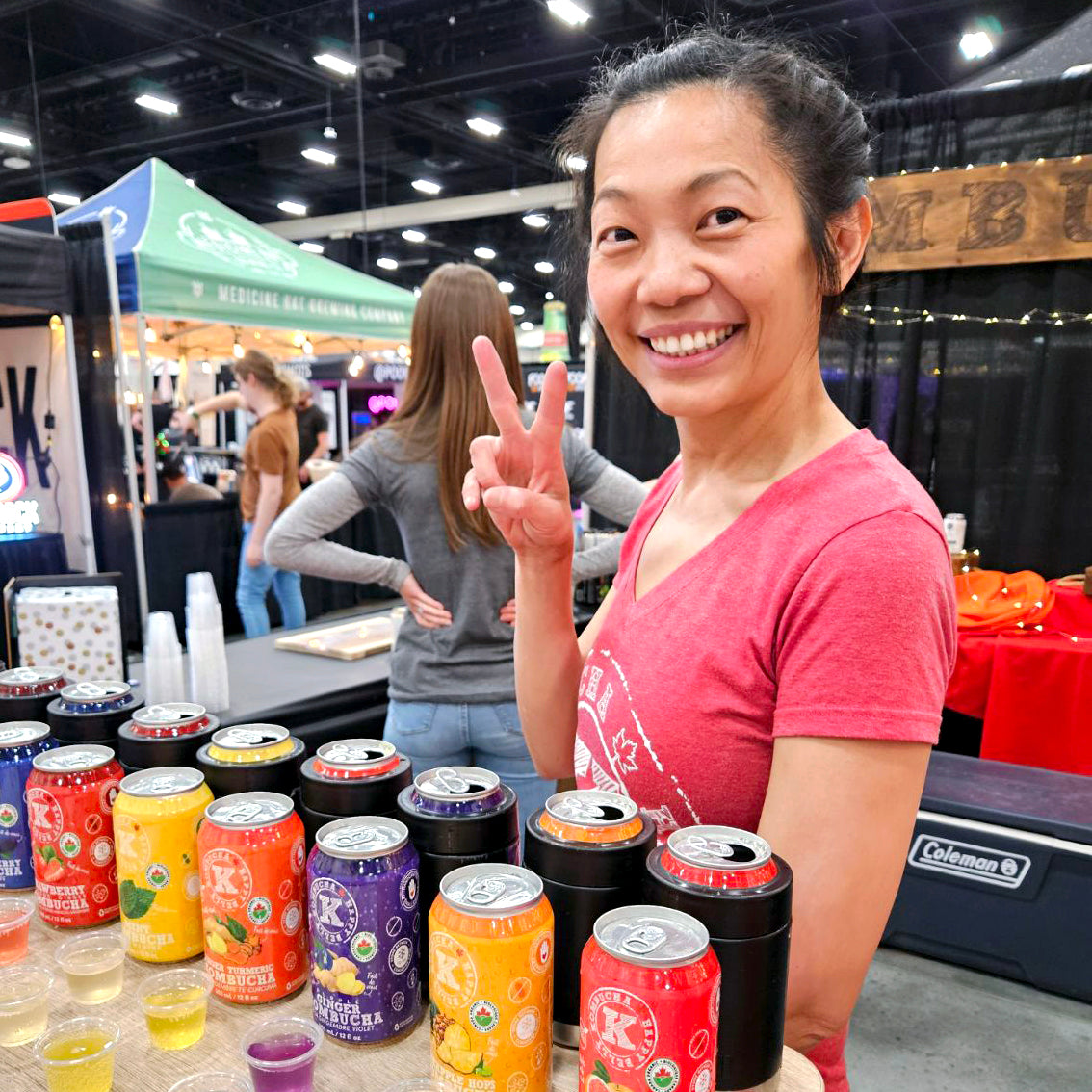 victoria the owner of happy belly kombucha with assorted cans of happy belly kombucha in a store fair